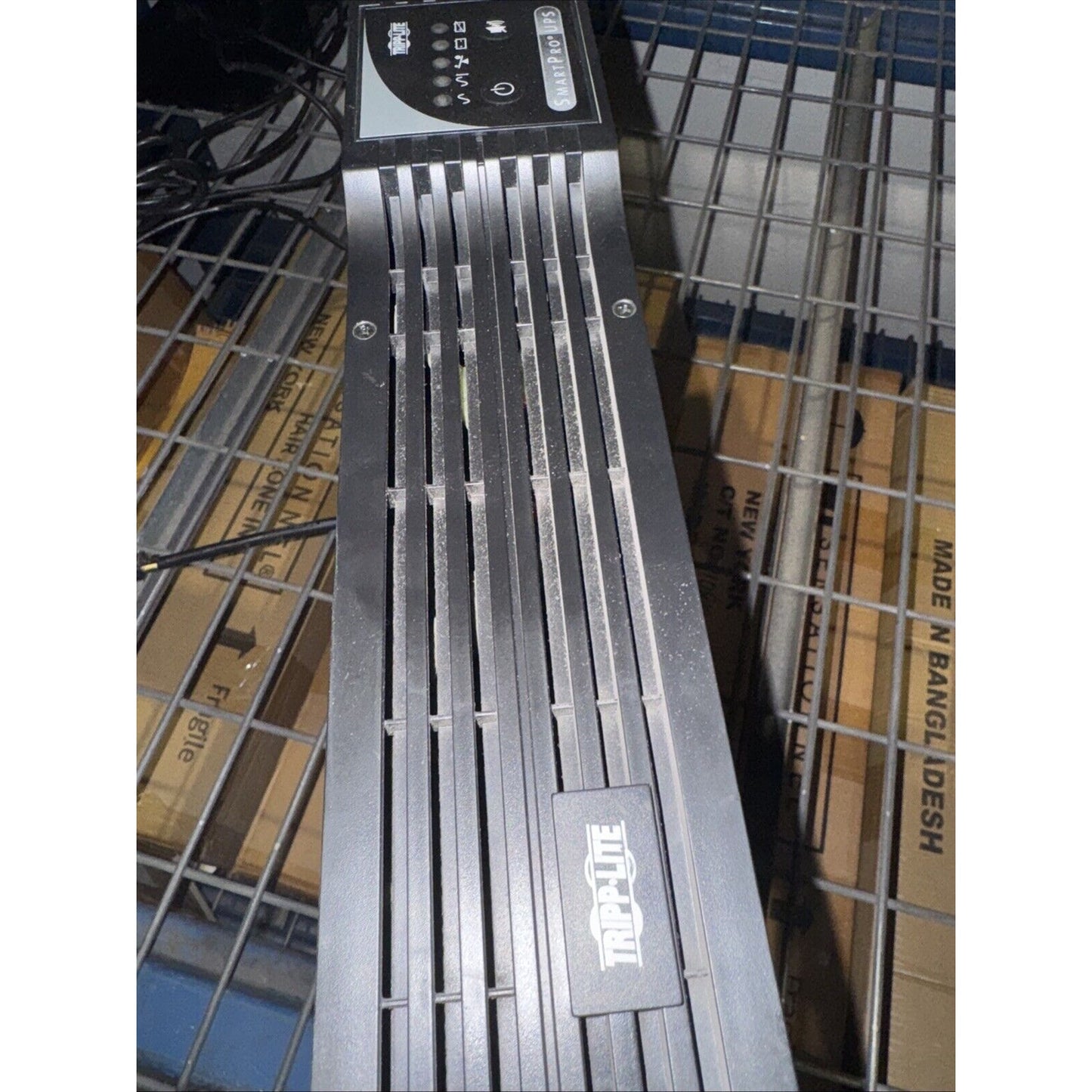 Tripp Lite SU1500RTXL2UA smart online UPS unit with vented front panel and control indicators on metal wire shelf