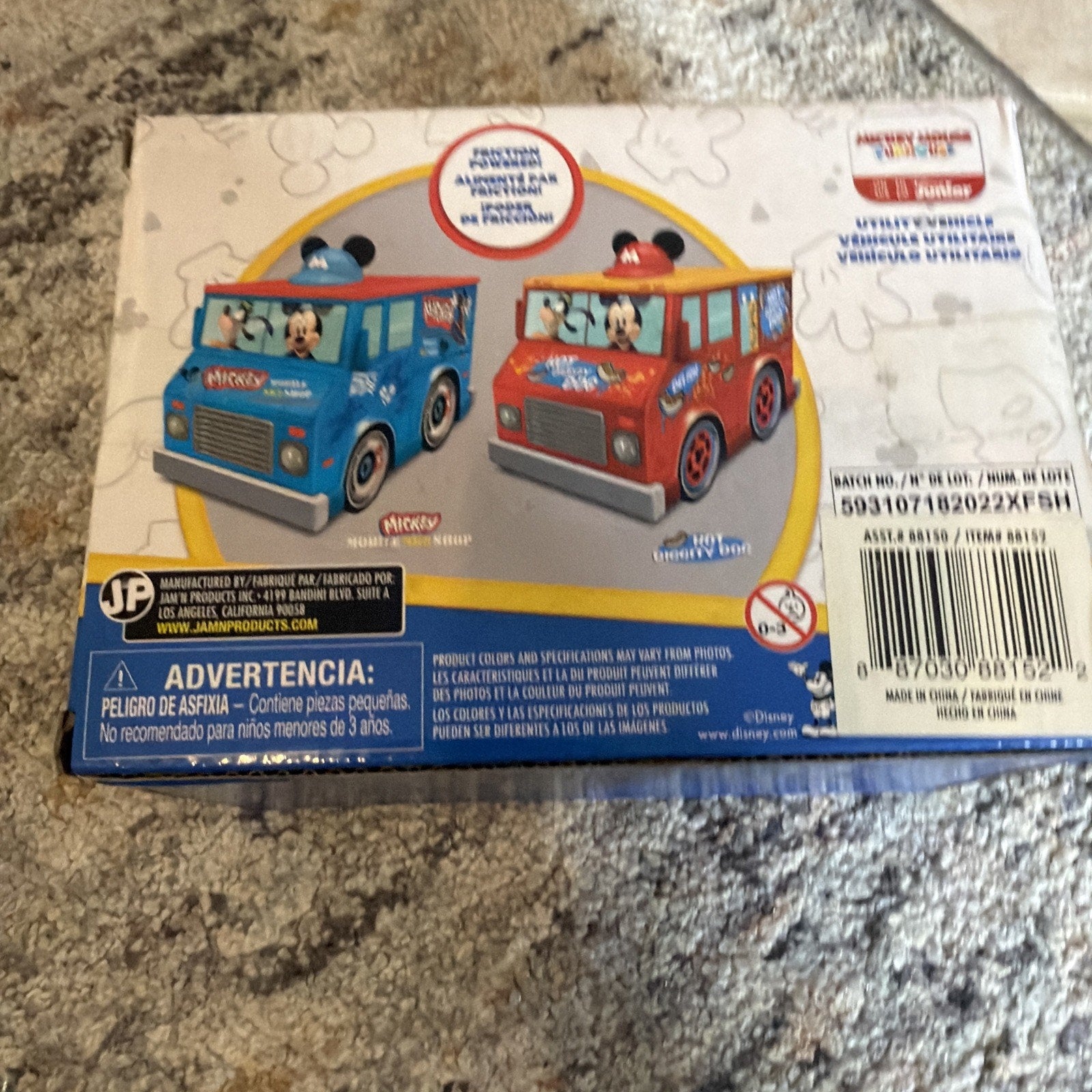 Box packaging displaying two small toy utility vehicles, one blue and one red, each adorned with Mickey Mouse graphics and ears on top, shown on a light background with faint Disney character outlines.