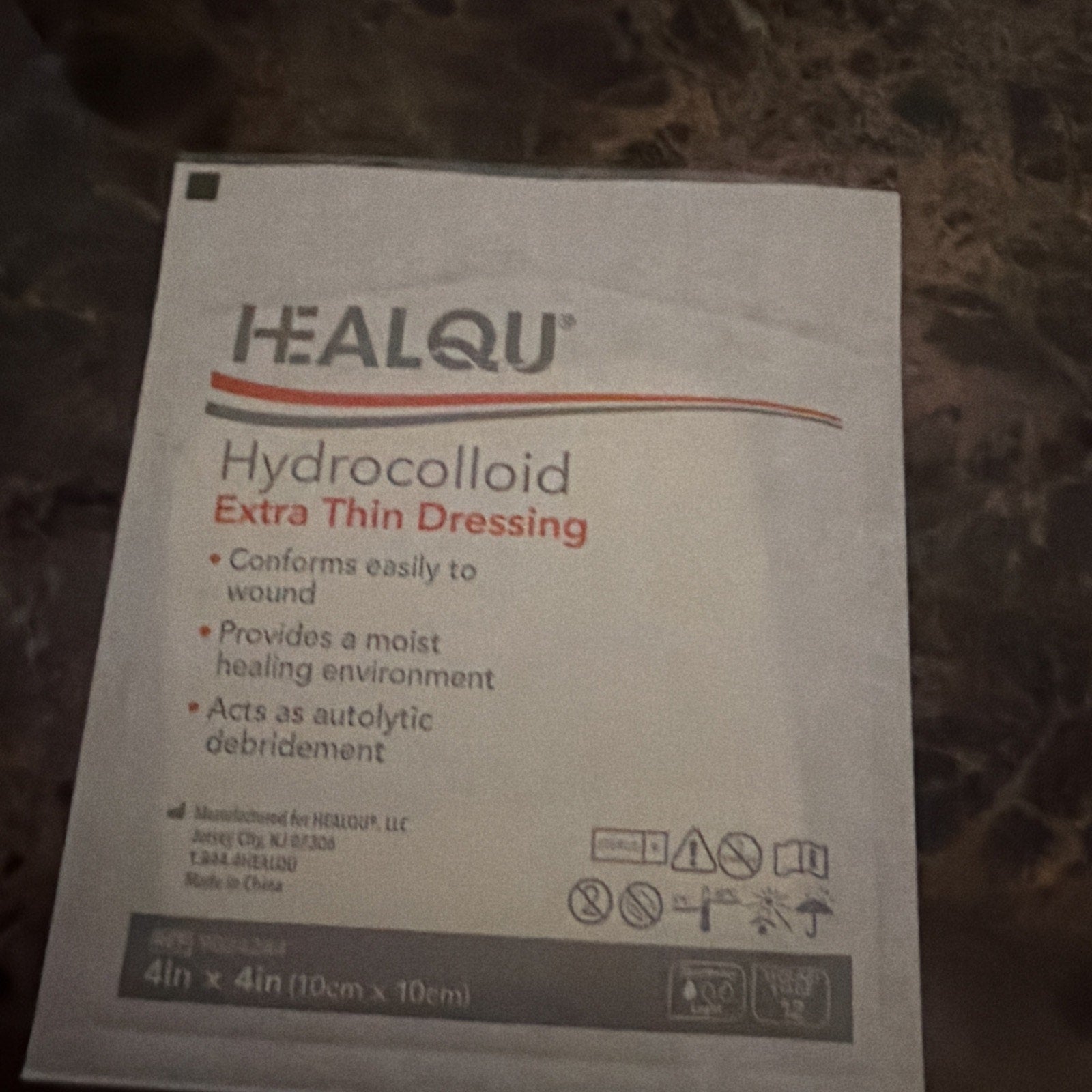 Single-use HEALQU hydrocolloid extra thin dressing packet with product benefits and usage instructions printed on a white packaging pouch placed on a textured dark surface.