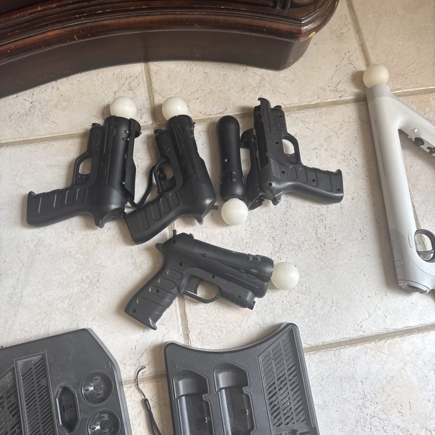 Two PlayStation VR black motion controllers and white gun attachments on tiled floor with accessory cases nearby