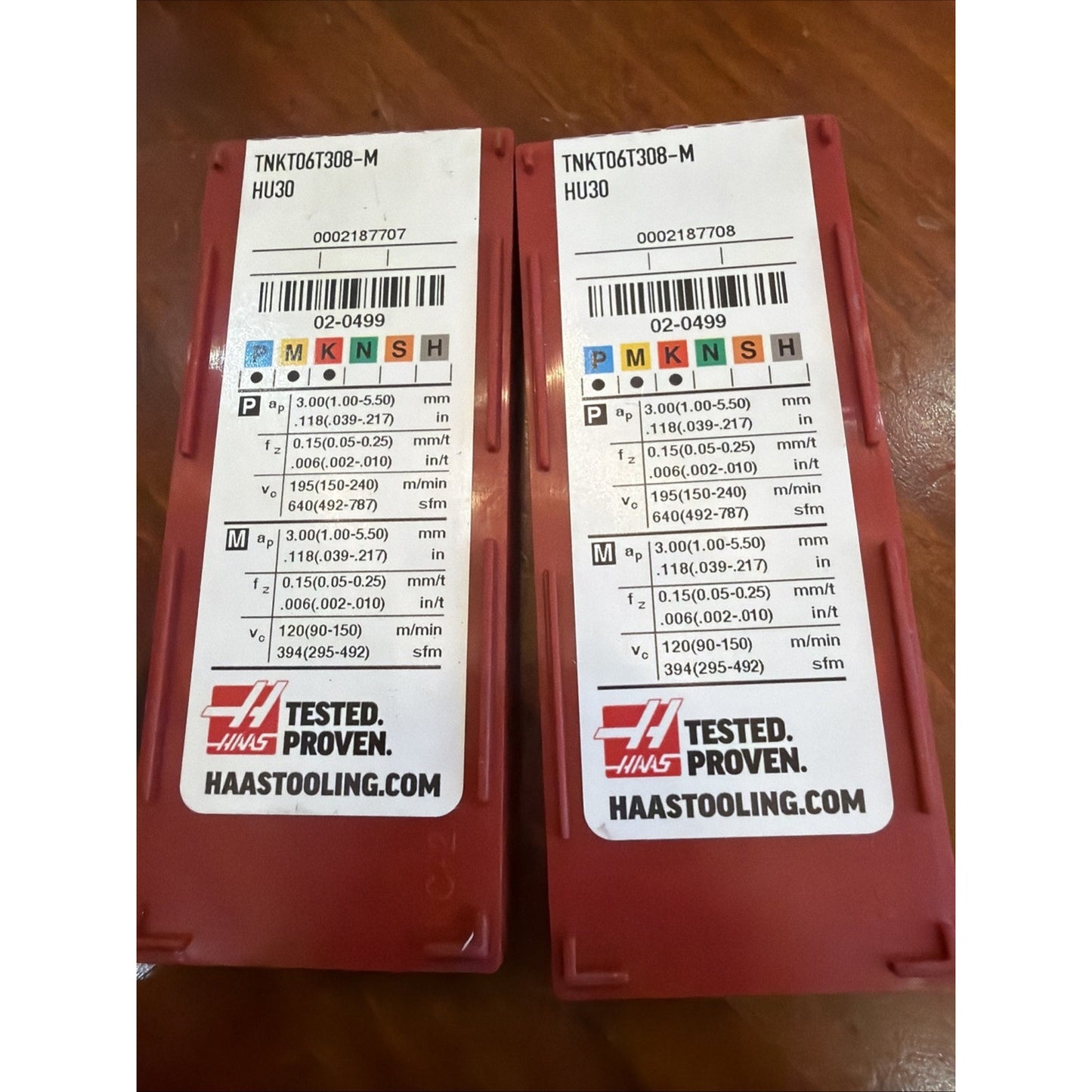 Two red plastic containers with identical white labels displaying technical specifications, barcodes, and the Haas logo, placed side by side on a wooden surface.