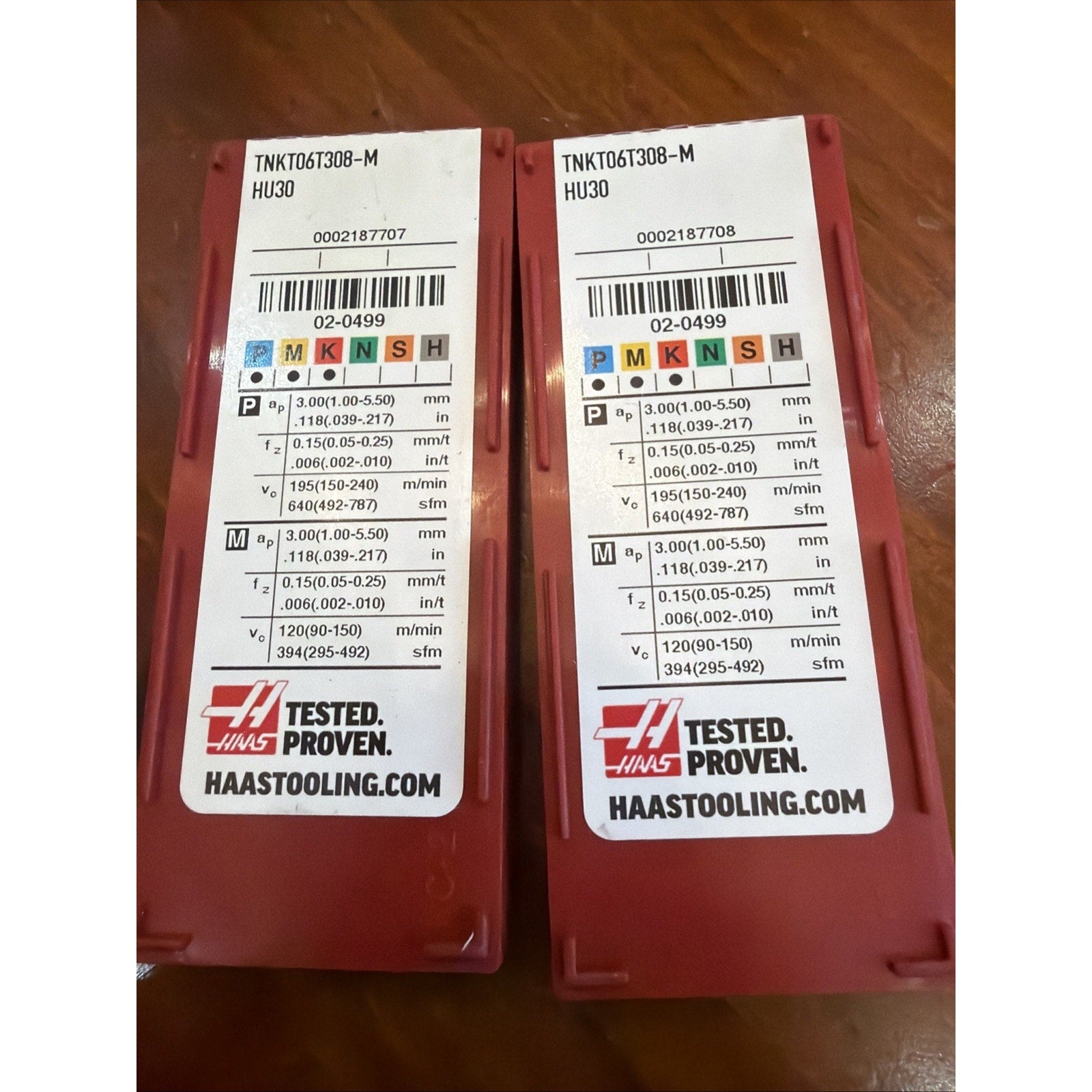 Two red plastic containers with identical white labels displaying technical specifications, barcodes, and the Haas logo, placed side by side on a wooden surface.