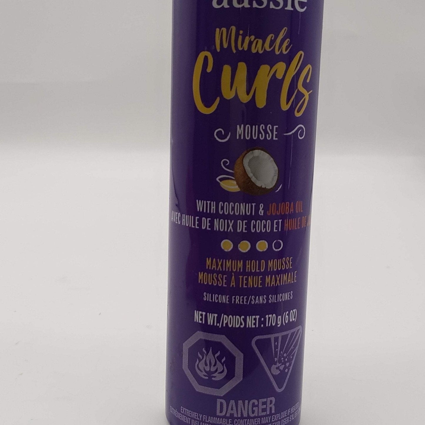 Tall purple aerosol can of styling mousse labeled Miracle Curls with coconut and jojoba oil, highlighting maximum hold and silicone-free formula, with hazard warnings at the bottom.