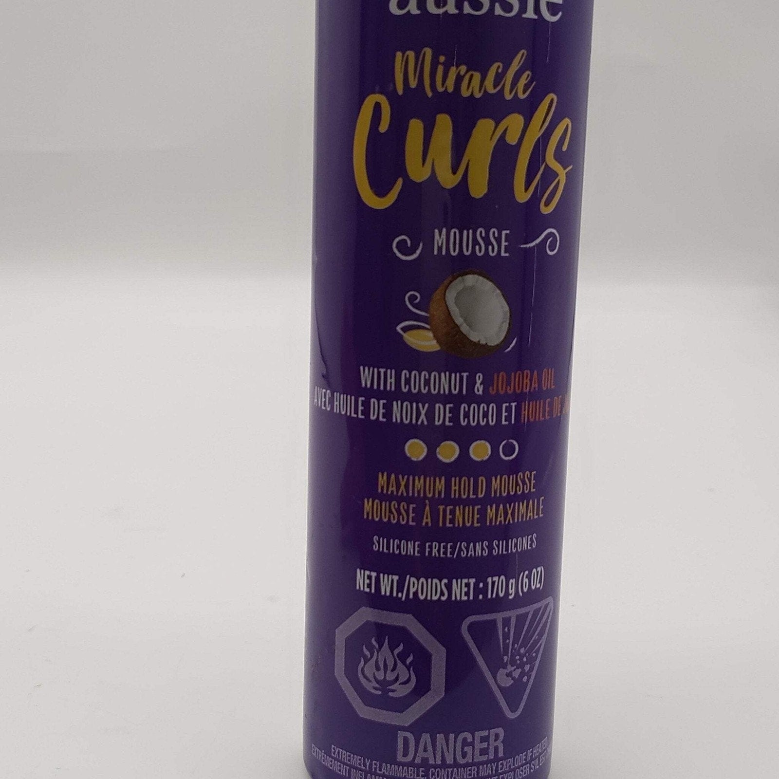 Tall purple aerosol can of styling mousse labeled Miracle Curls with coconut and jojoba oil, highlighting maximum hold and silicone-free formula, with hazard warnings at the bottom.