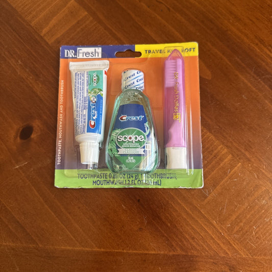 Dr. Fresh Travel Kit with Crest toothpaste, Scope mouthwash, and pink toothbrush in blister pack on wood surface