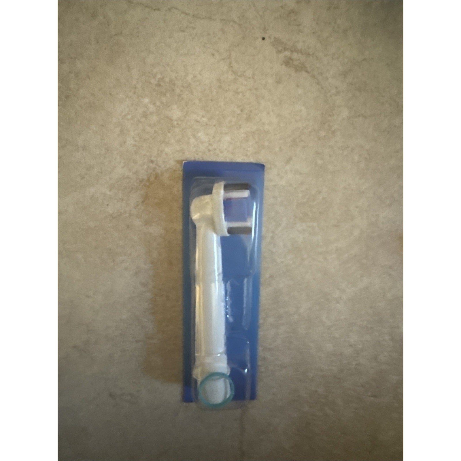 Single Oral-B electric toothbrush replacement head in clear plastic packaging on beige surface