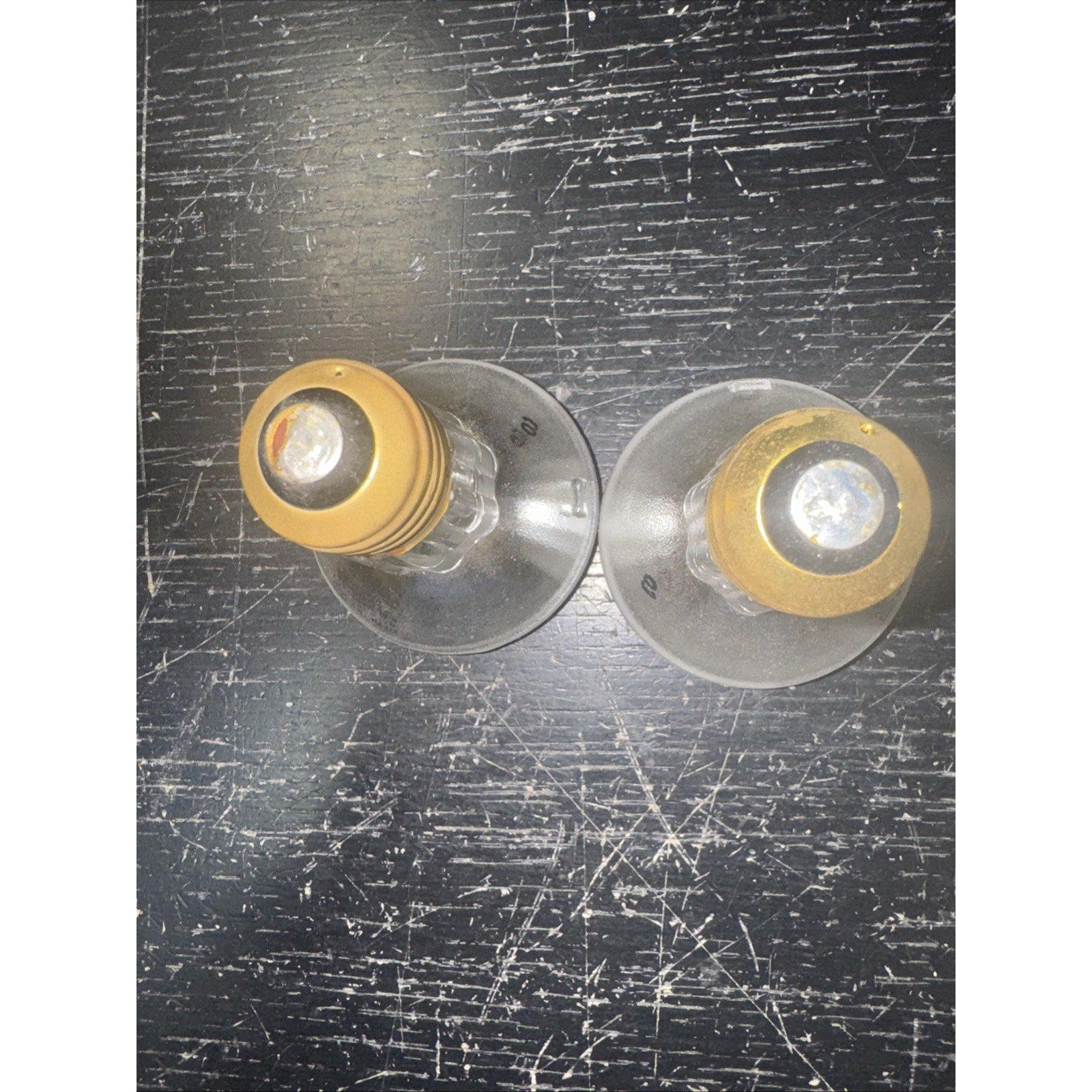 Two replacement 50PAR20/H/FL 120V 50W light bulbs with gold base on scratched black surface