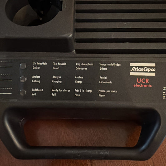Atlas Copco UCR electronic power tool battery charger with multilingual status indicators and black carrying handle