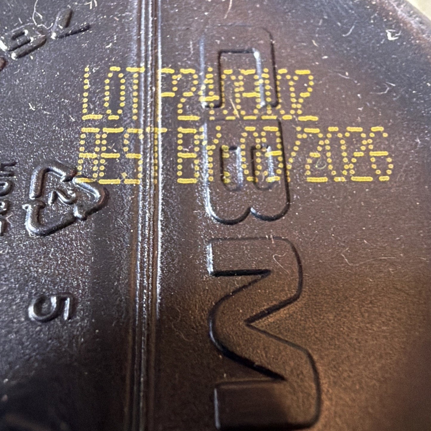 Close-up of a textured black surface with yellow printed lot number P24012 and expiration date 07/10/2026, showing molded recycling symbol and partial embossed letters.