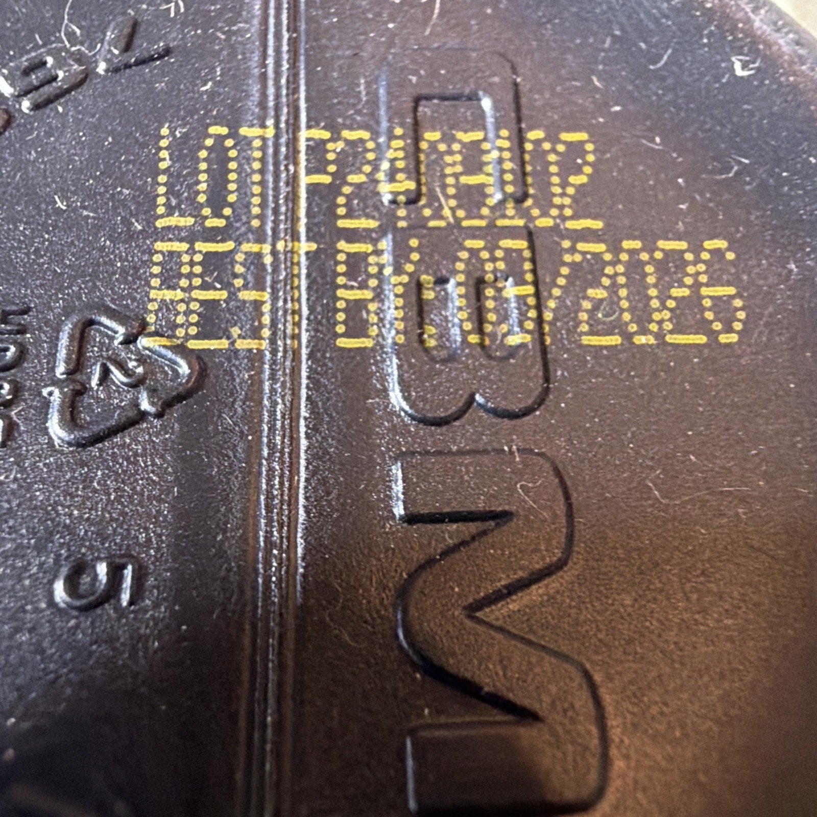 Close-up of a textured black surface with yellow printed lot number P24012 and expiration date 07/10/2026, showing molded recycling symbol and partial embossed letters.