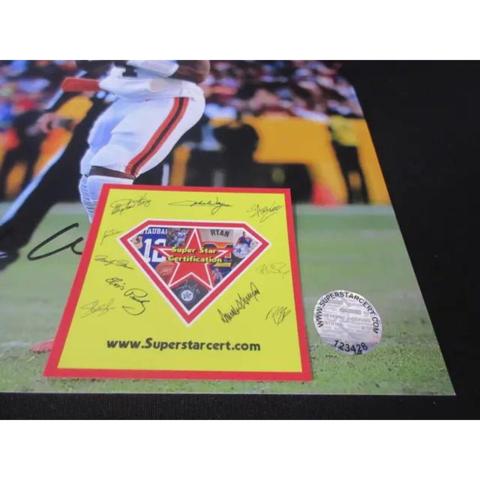 Close-up of a yellow and red Super Star Certification sticker with multiple signatures and a holographic authenticity seal on a sports photograph showing a football player’s leg on a grassy field.