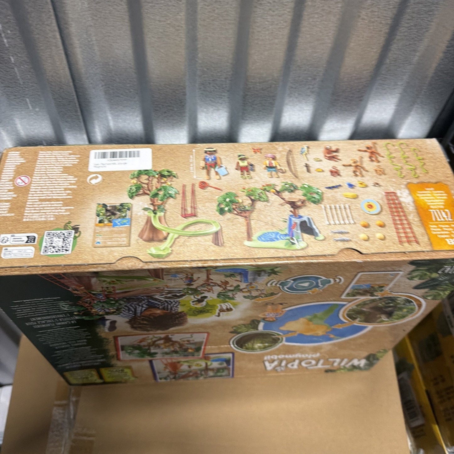 Top view of a toy set box showing illustrations of jungle trees, a slide, water feature, fencing, animal figures, and human figurines designed for imaginative wildlife play.