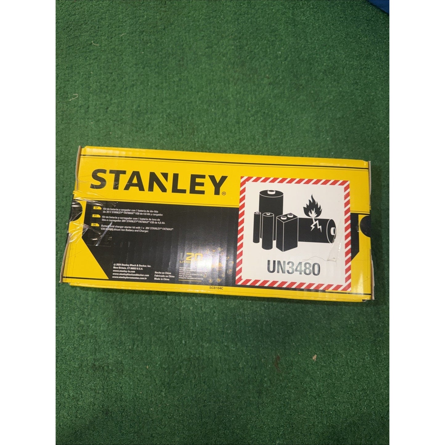 Yellow and black Stanley branded packaging box featuring a warning label for lithium-ion batteries with a flame symbol and UN3480 code on a green fabric background.