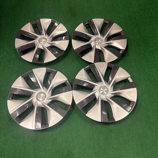 Set of four silver and black plastic wheel covers with a modern geometric design, arranged on a green carpeted surface.