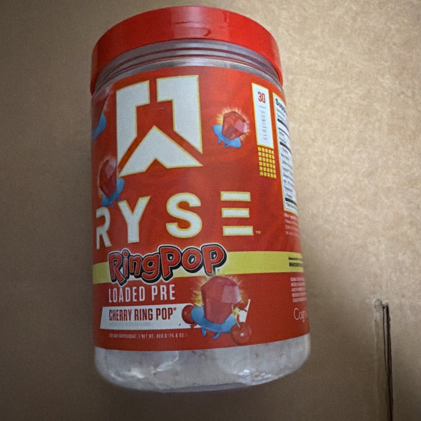 Red plastic container of Ryse brand Ring Pop Loaded Pre workout supplement in Cherry Ring Pop flavor, featuring vibrant colorful graphics and nutrition facts on the side.