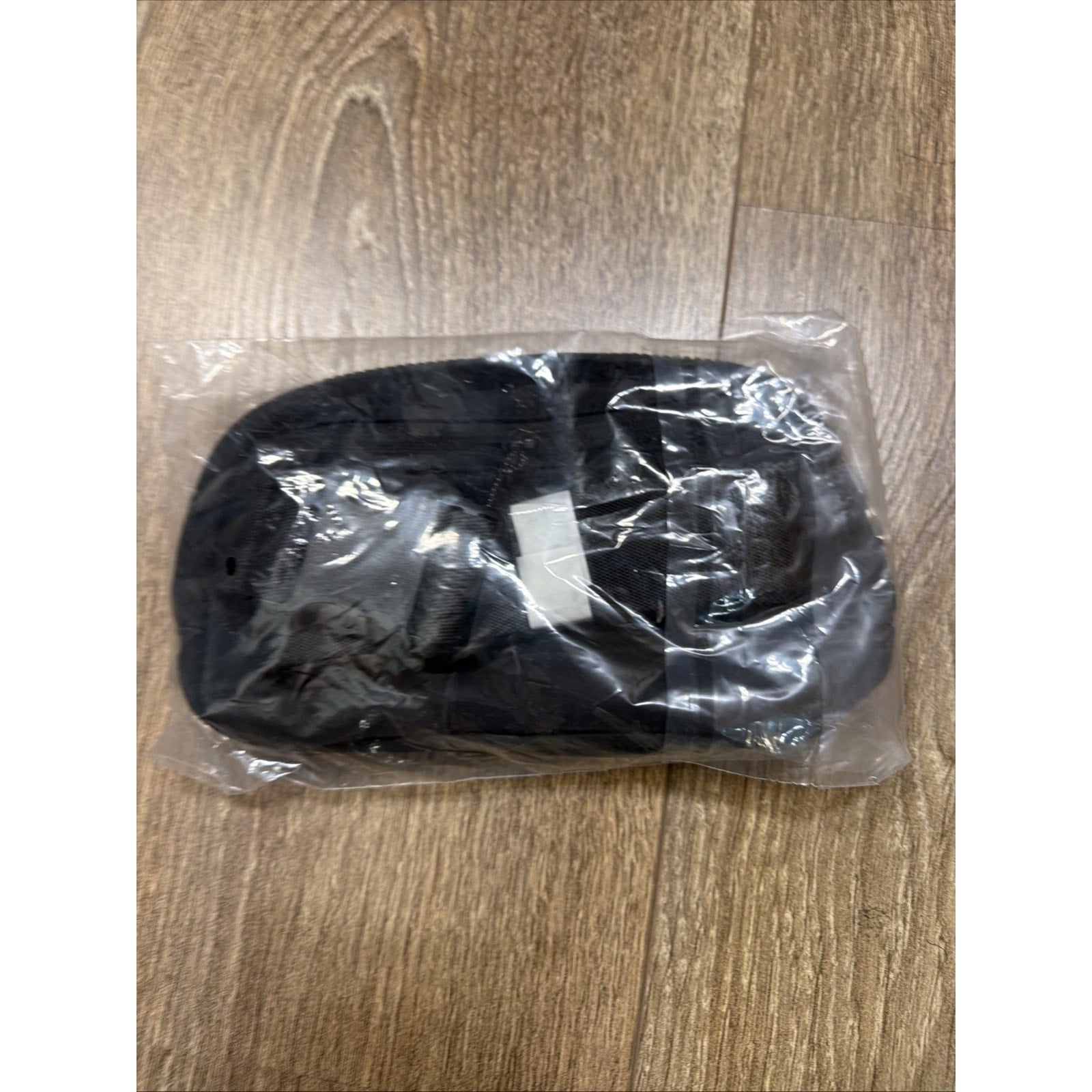 Black fabric pouch with zipper closure, packaged inside a clear plastic bag, placed on a wooden floor surface.