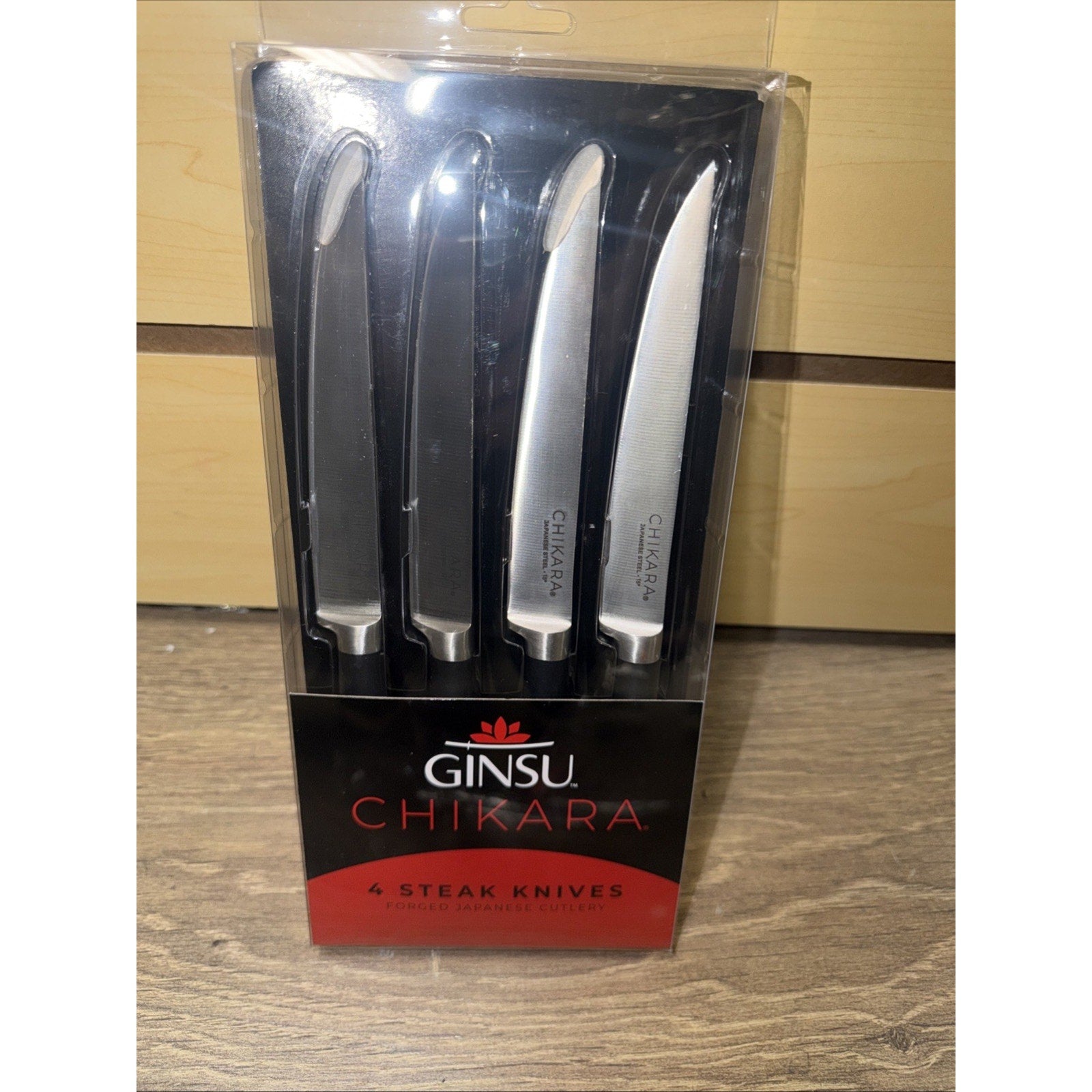 Set of four Ginsu Chikara steak knives with stainless steel blades and black handles, packaged in a clear plastic case with red and black labeling.
