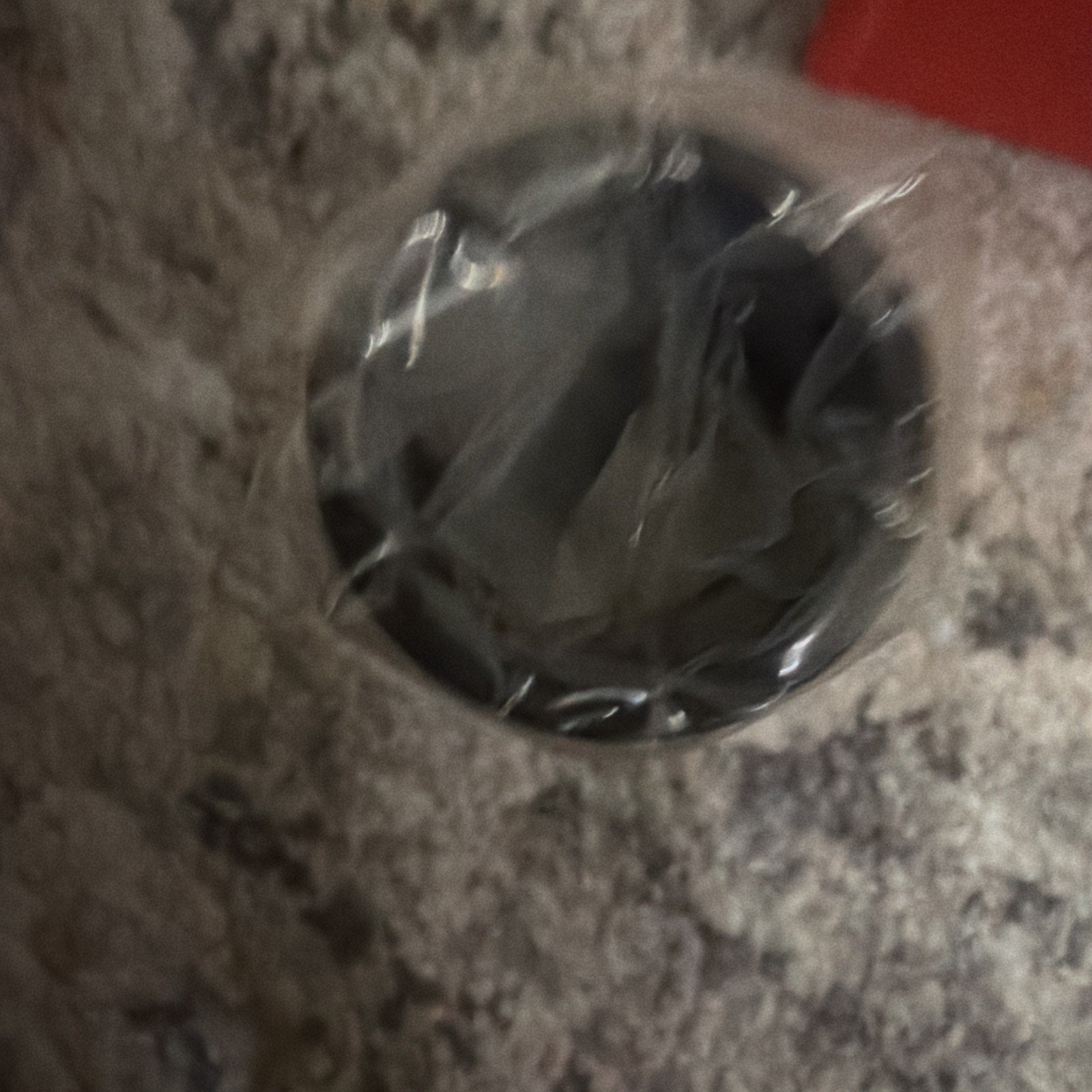 Blurred close-up of a cylindrical object wrapped in transparent plastic, placed on a textured, light-colored carpet surface.
