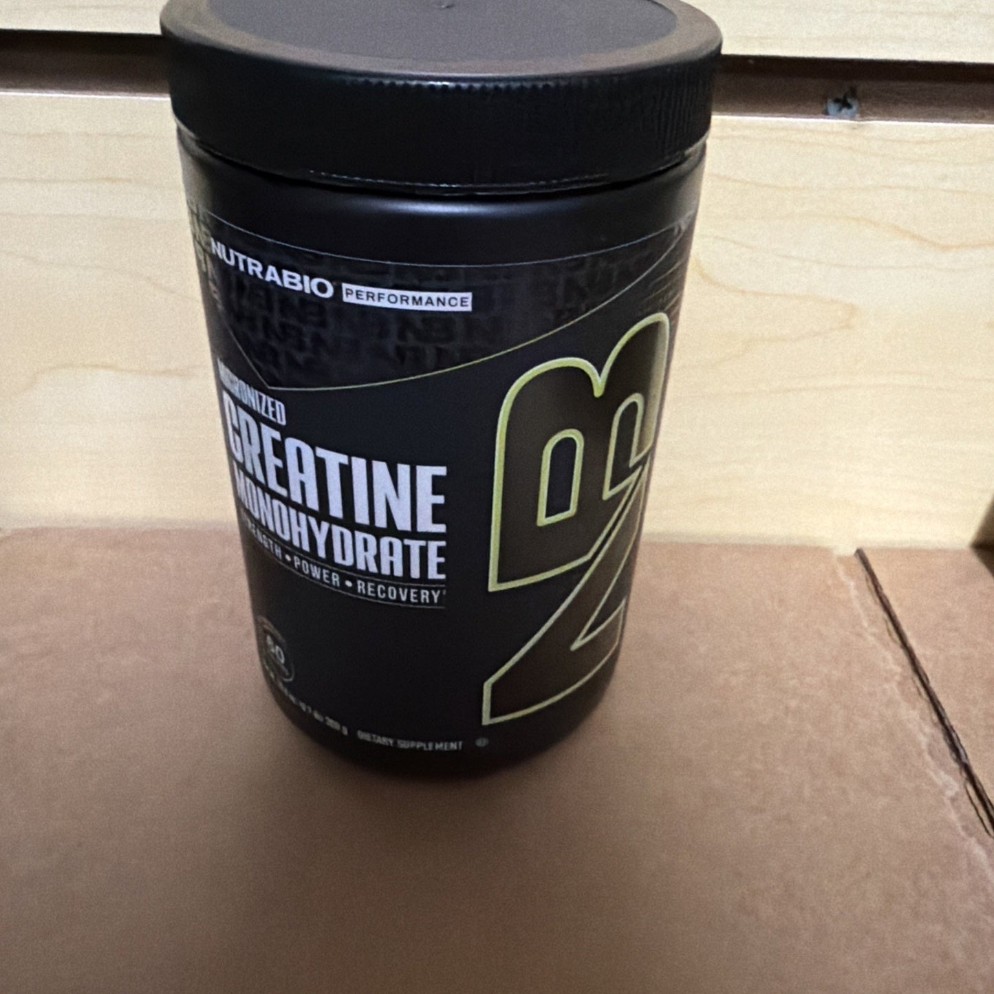 Black plastic container of Nutrabolt branded creatine monohydrate supplement with bold yellow and white text on the label, placed on a wooden surface.