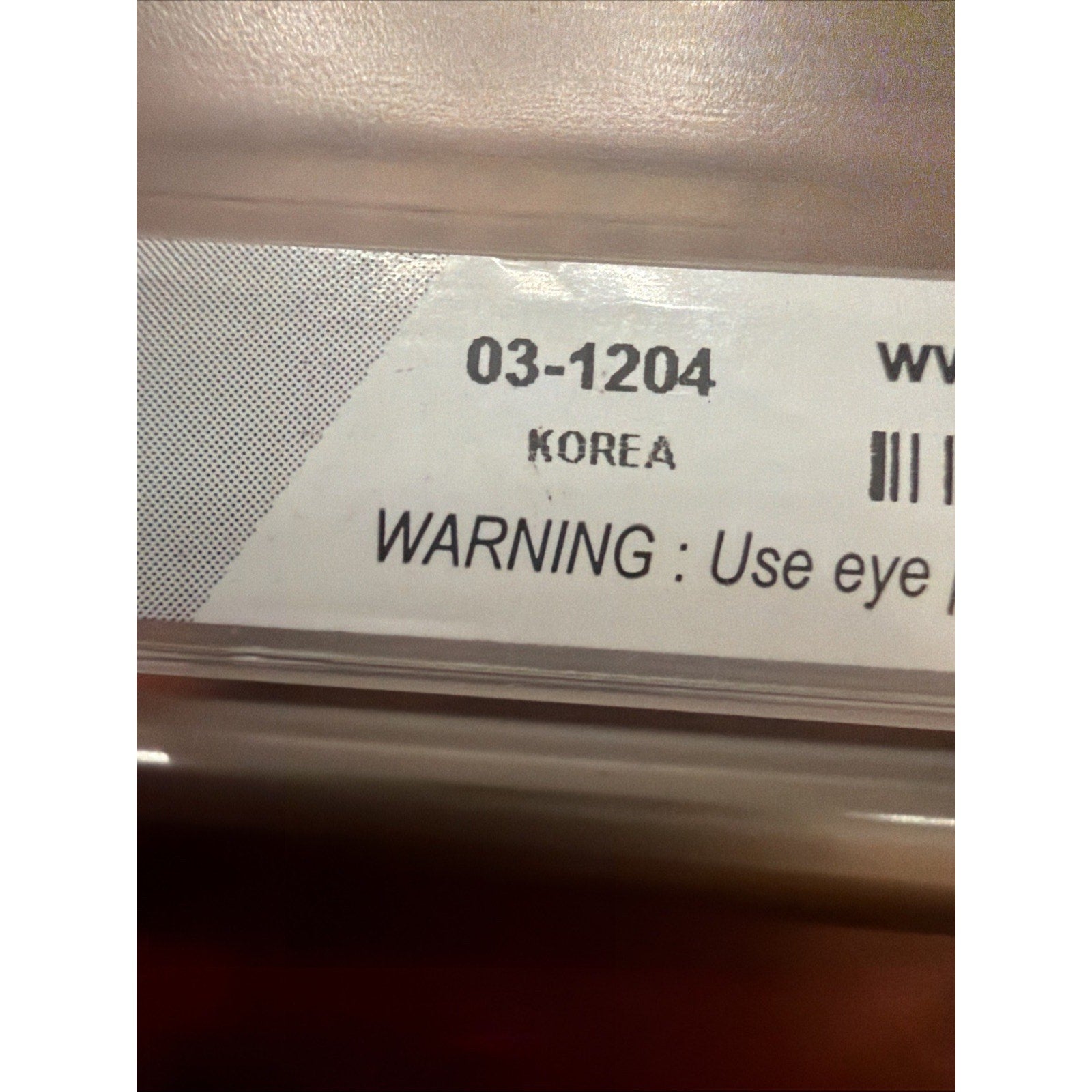 Close-up of a product label displaying code 03-1204, origin marked as Korea, and a safety warning advising the use of eye protection.
