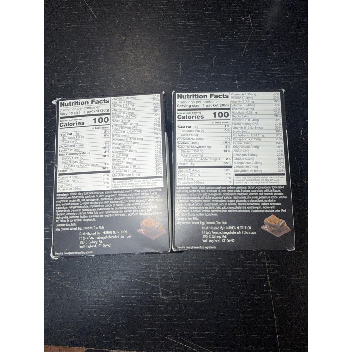 Two nutrition facts labels for chocolate snacks, each showing 100 calories per serving, detailed macronutrients, vitamins, minerals, and ingredients on black packaging against a dark wooden surface.
