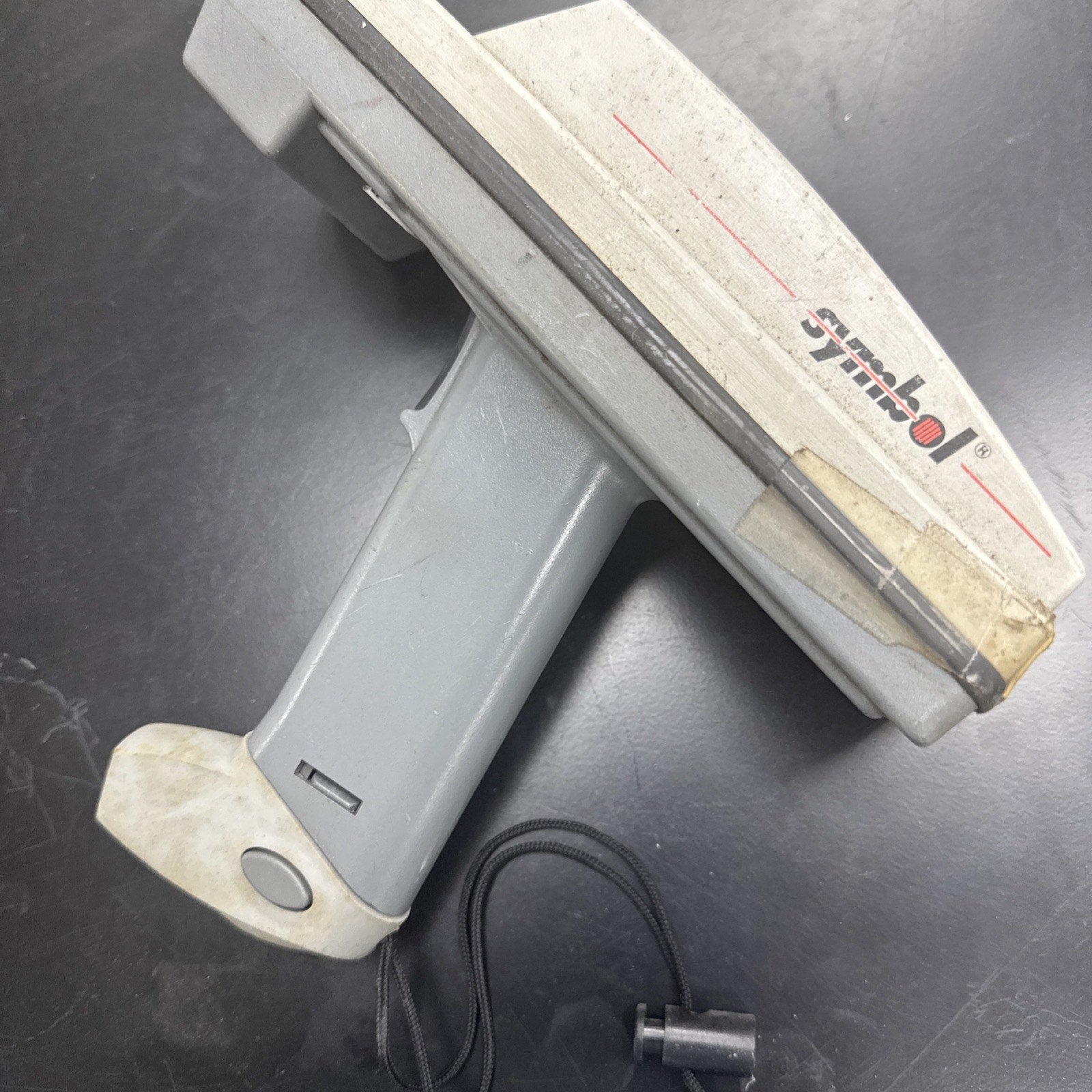 Used Symbol barcode scanner with ergonomic gray handle and white top housing on black surface with attached cable