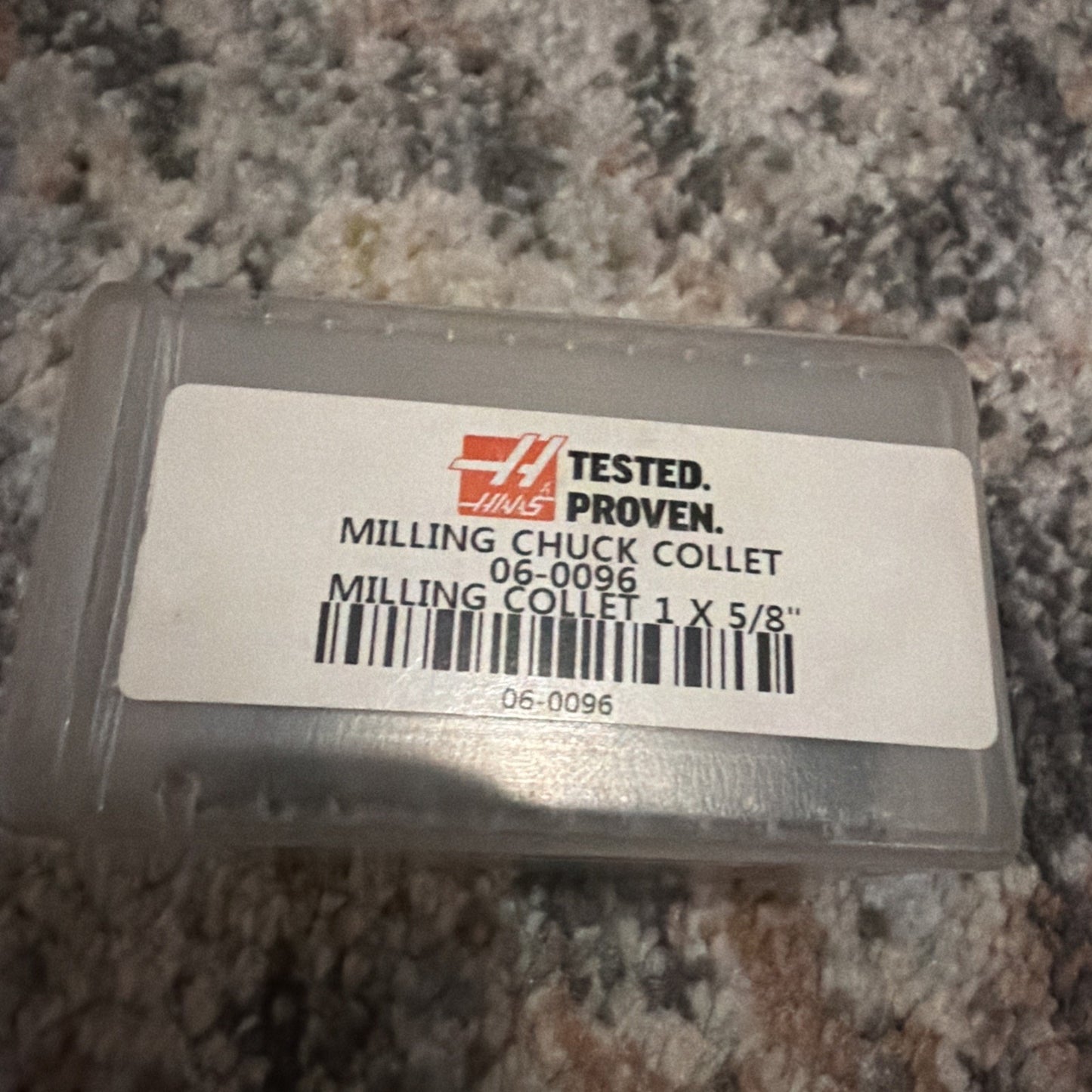 Transparent plastic case with a white label featuring the Haas logo and product details for a milling chuck collet size 1 x 5/8 inch, placed on a multicolor carpet surface.