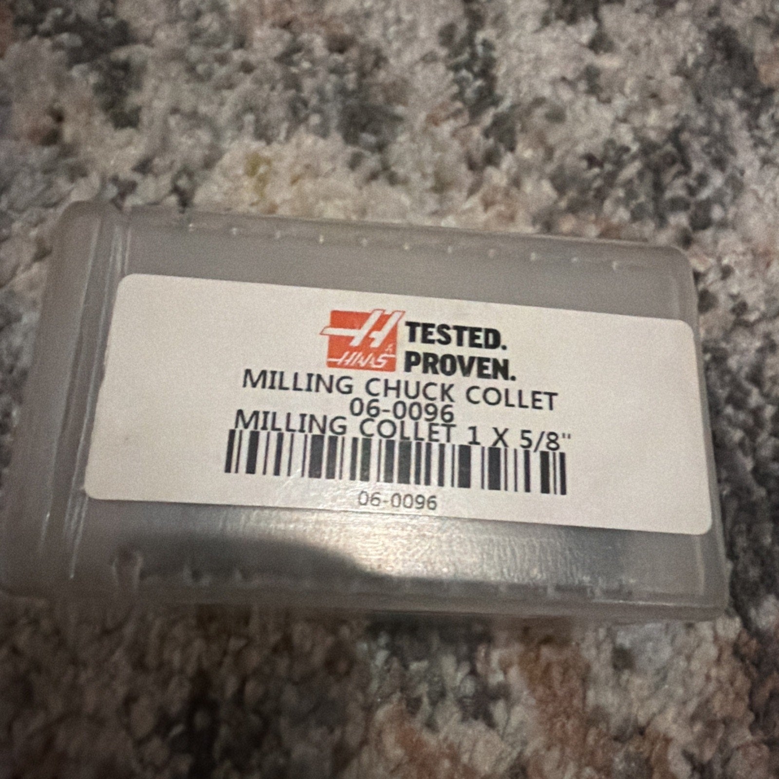 Transparent plastic case with a white label featuring the Haas logo and product details for a milling chuck collet size 1 x 5/8 inch, placed on a multicolor carpet surface.