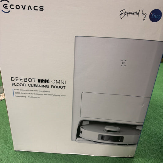 Packaging box showing a white floor cleaning robot partially visible from its storage station, featuring branding and product details on a white background with a green carpet underneath.