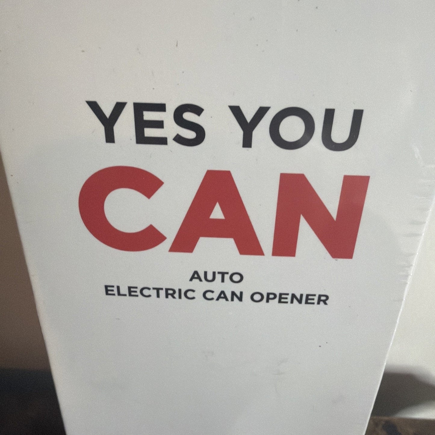 White box with bold text in black and red reading "YES YOU CAN" and smaller text below stating "AUTO ELECTRIC CAN OPENER" on a plain background.