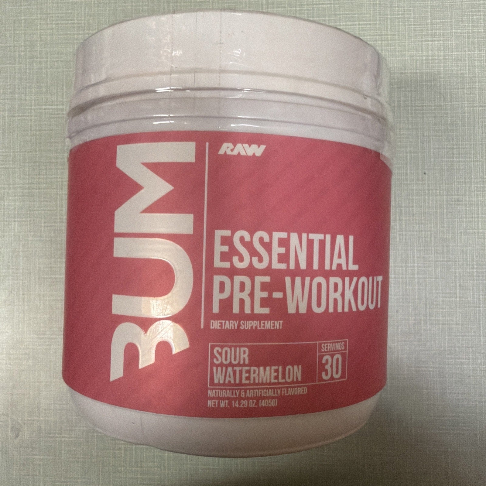 White plastic container of RAW RUM Essential Pre-Workout dietary supplement in sour watermelon flavor, featuring a pink label with serving size of 30 and flavor details.