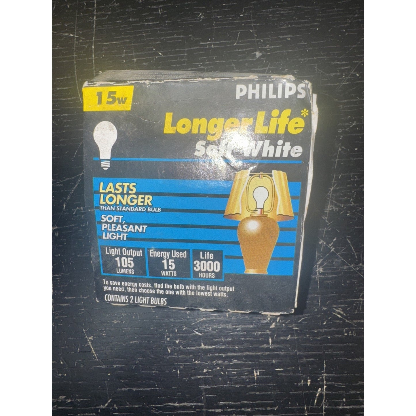 Philips 15W Longer Life Soft White light bulbs box with specs and illustration of lamp on black surface