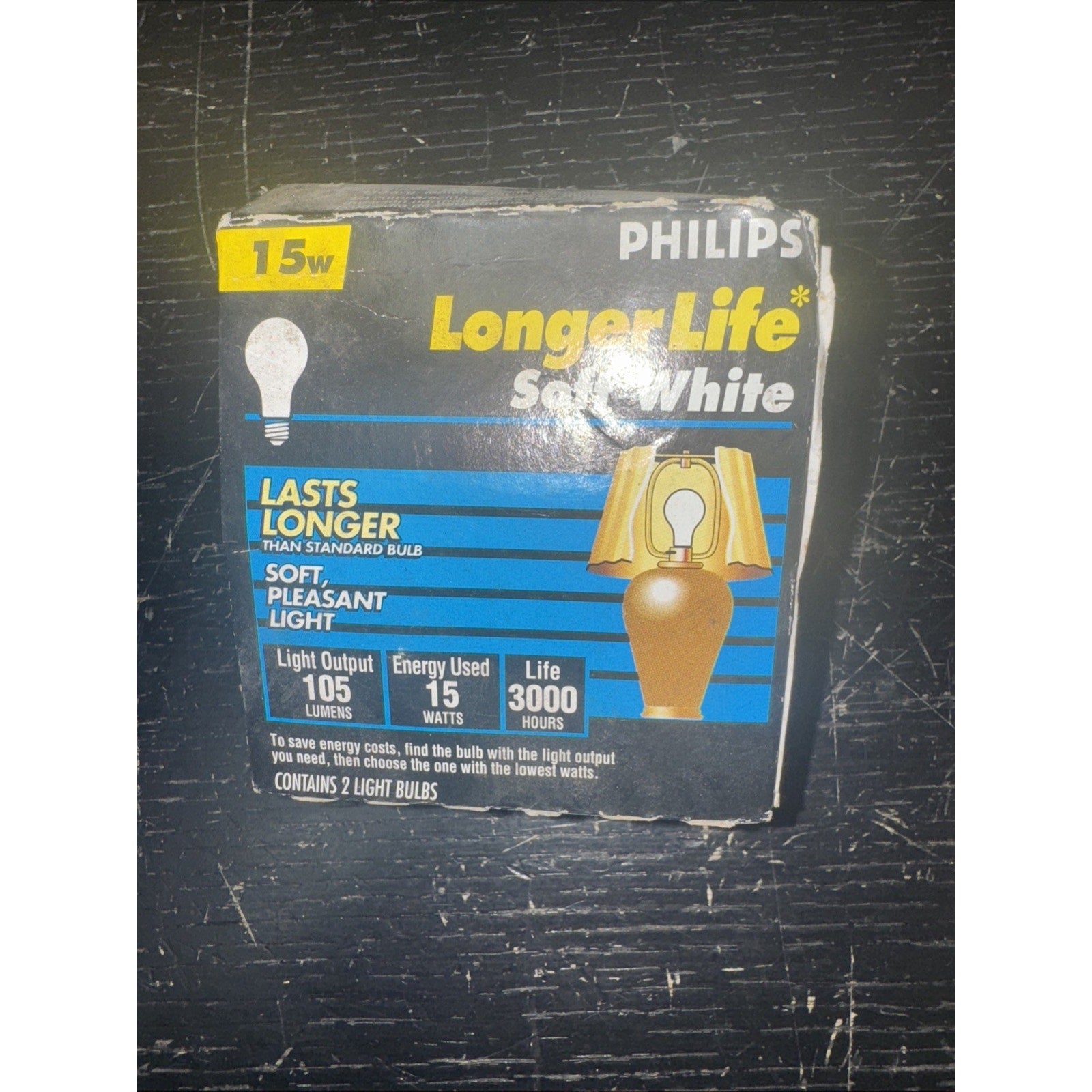 Philips 15W Longer Life Soft White light bulbs box with specs and illustration of lamp on black surface