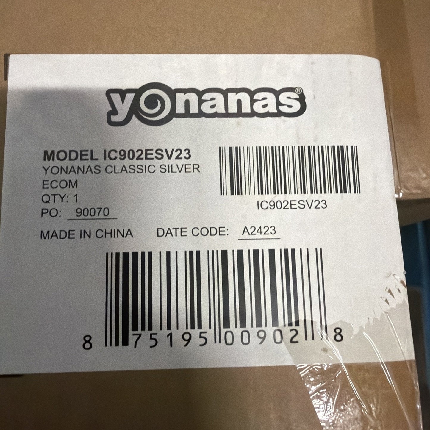 Close-up of a white product label on cardboard featuring the Yonanas logo, model number IC902ESV23, barcode, quantity, purchase order number, country of manufacture, and date code.