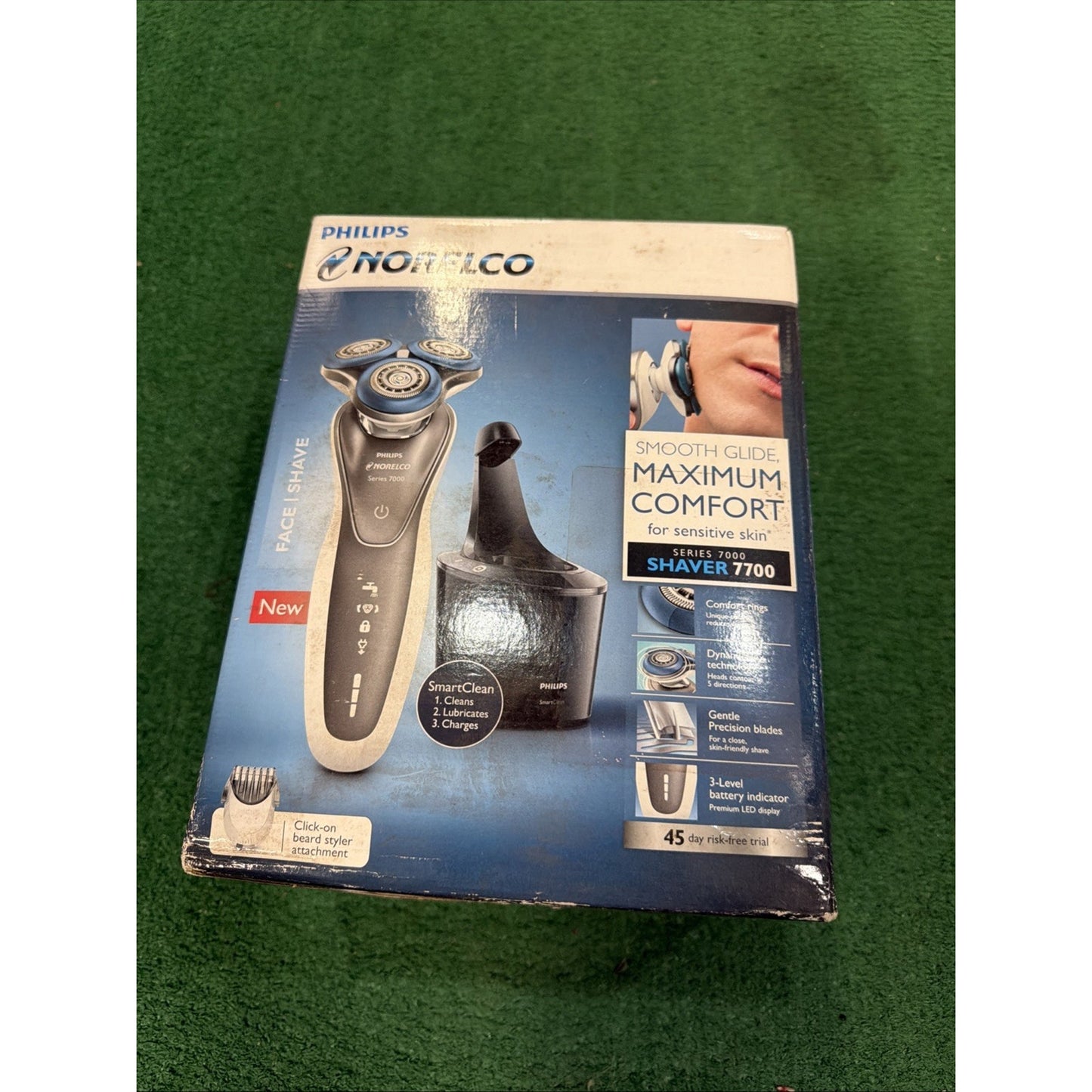 Box featuring a Philips Norelco electric shaver with three rotary blades, charging stand, and click-on beard styler, displayed on a blue and white background.