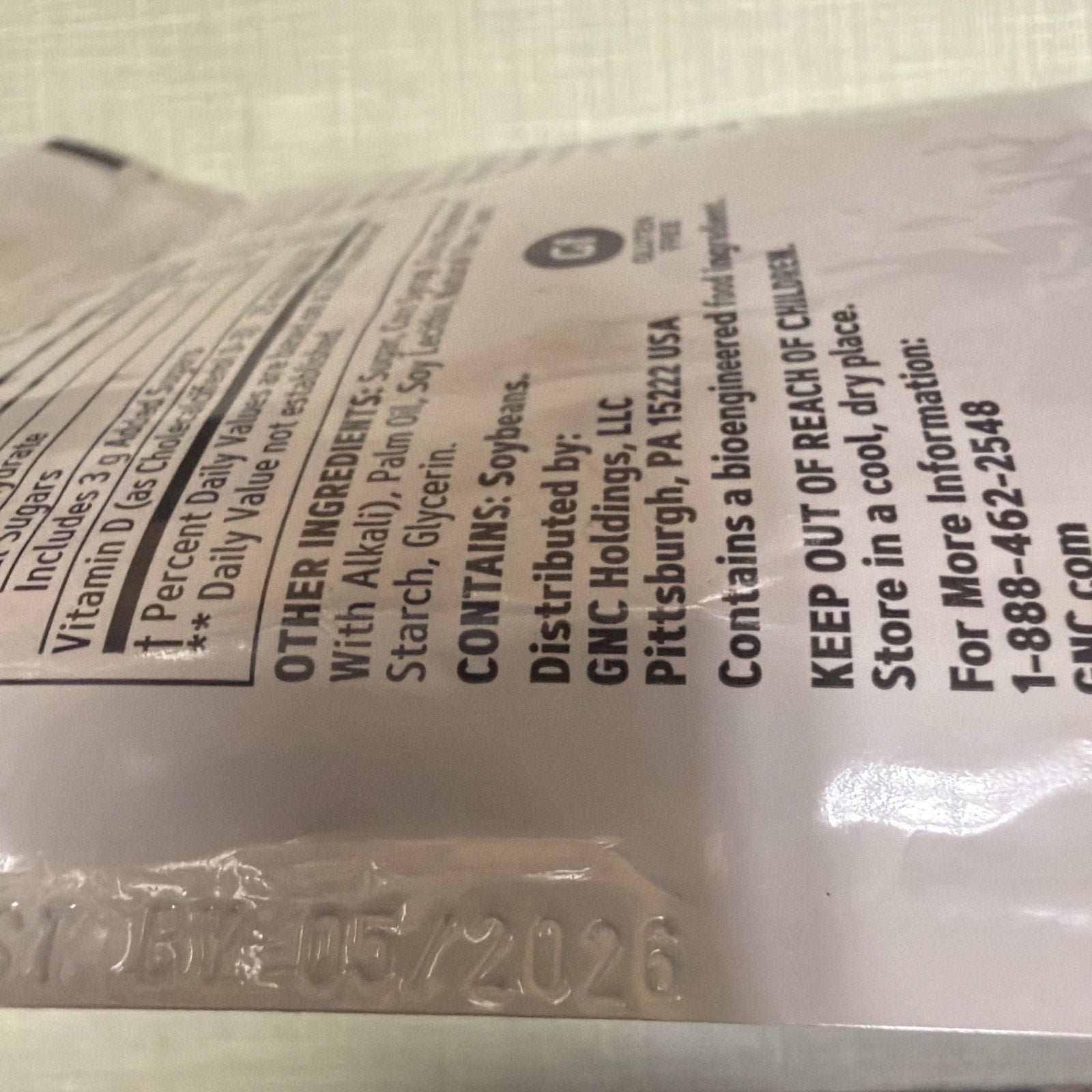 Close-up of a light-colored supplement pouch showing ingredient list including palm oil and soybeans, distributor information from Pittsburgh, and safety instructions to keep out of reach of children.