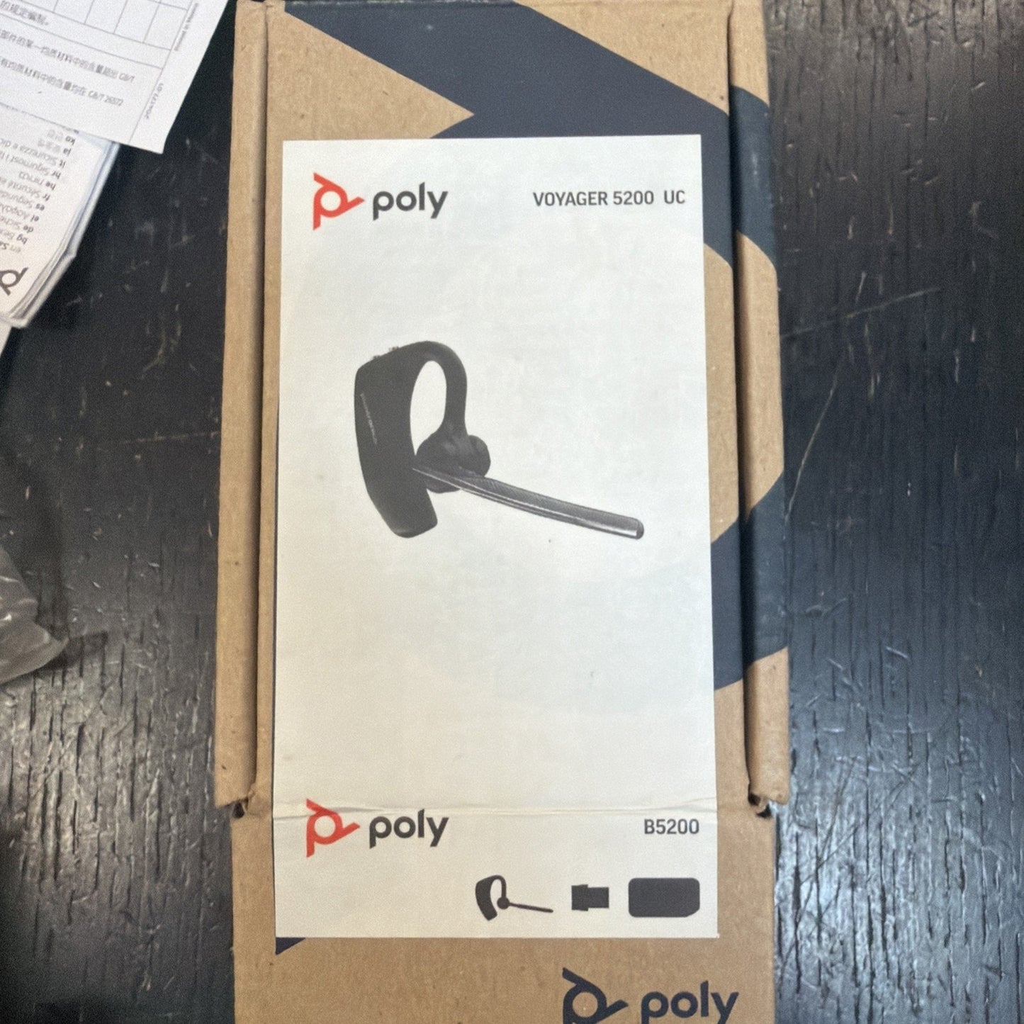 Cardboard box featuring a printed label with an image of a black over-the-ear headset with a boom microphone, labeled as the Poly Voyager 5200 UC.