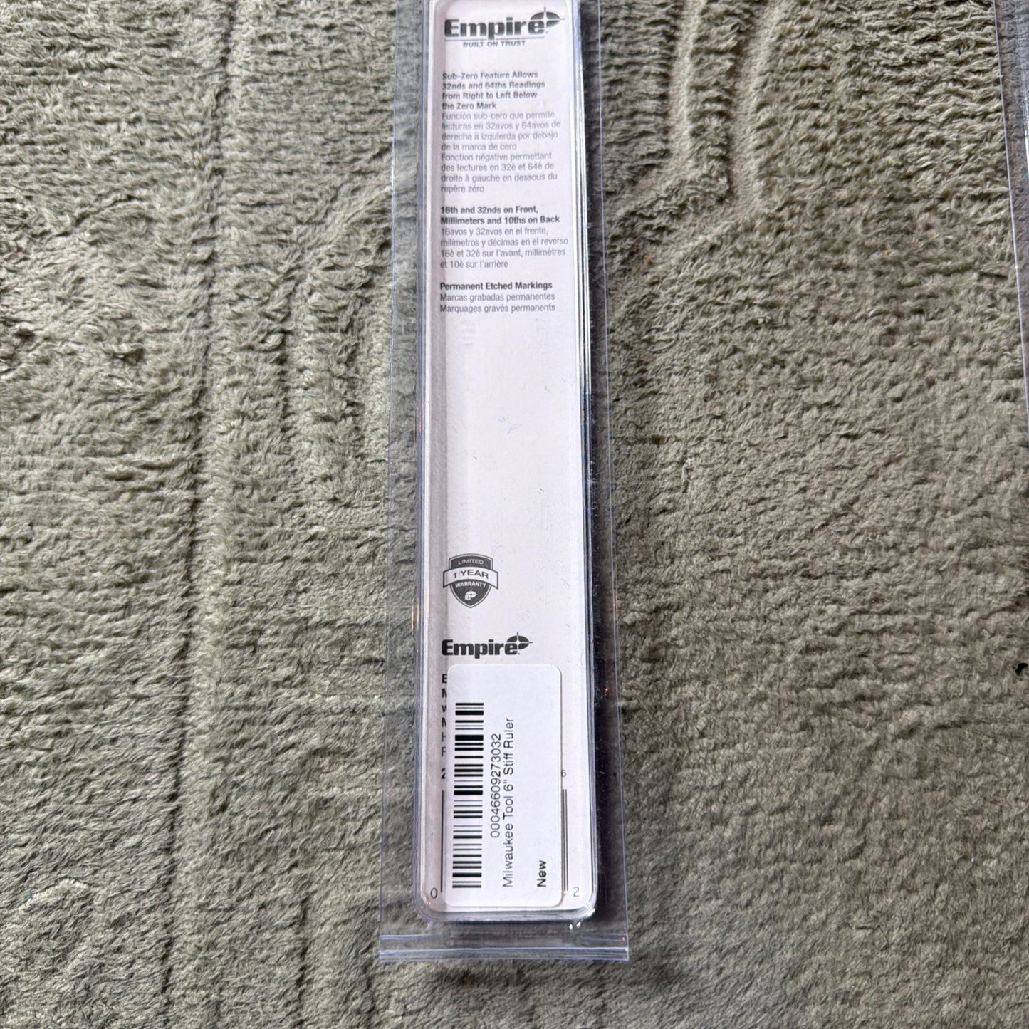 Clear plastic packaging containing a steel ruler with Empire branding, featuring product information and barcode label on a white backing, placed on a textured beige carpet.