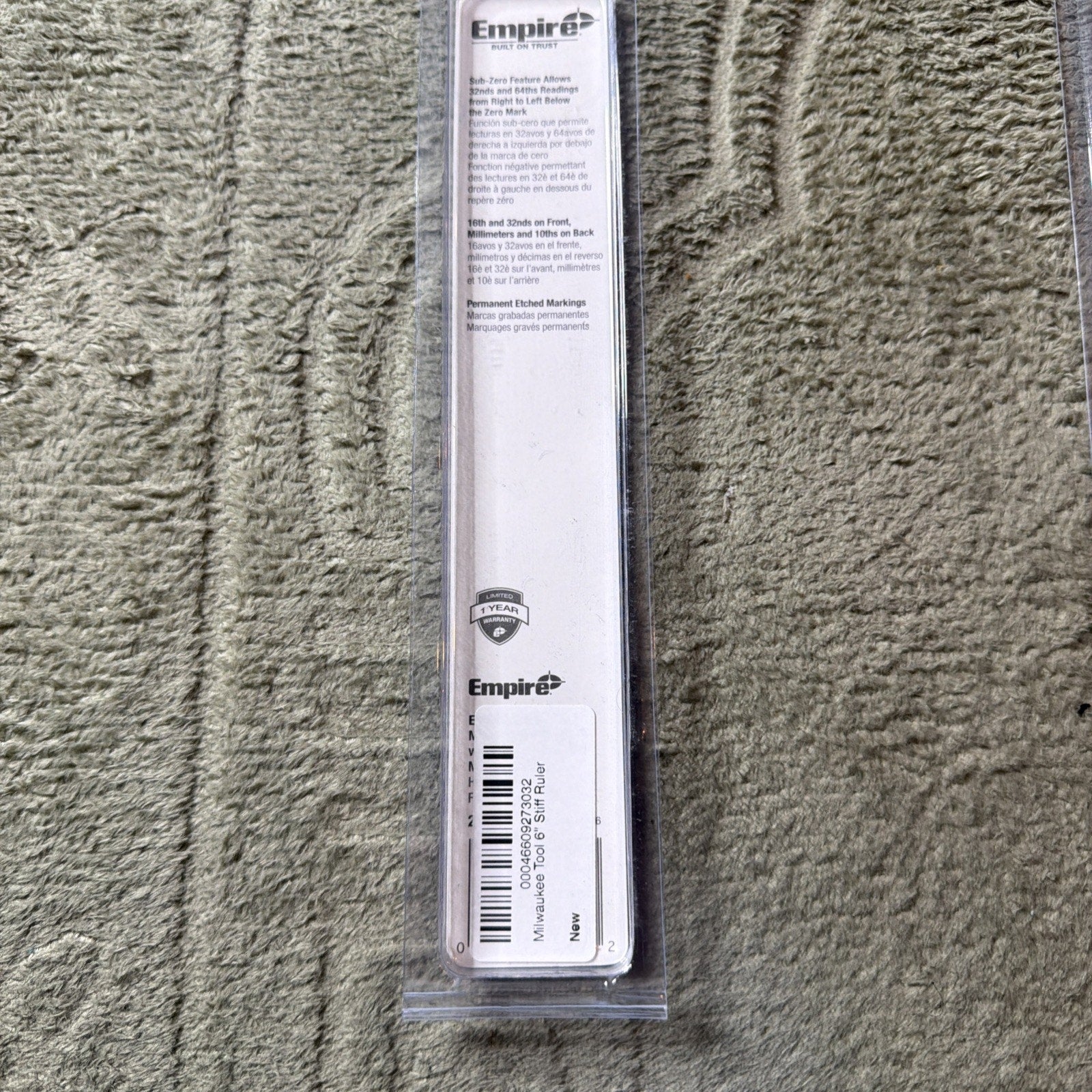 Clear plastic packaging containing a steel ruler with Empire branding, featuring product information and barcode label on a white backing, placed on a textured beige carpet.