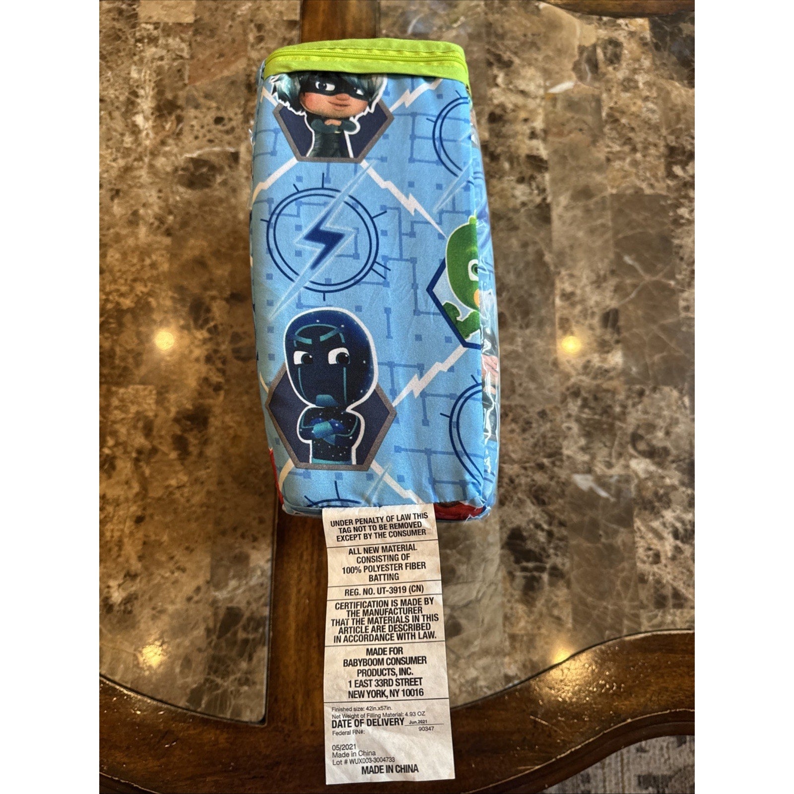 PJ Masks toddler bed bedding set folded showing colorful character prints with sewn label tag on marble table surface