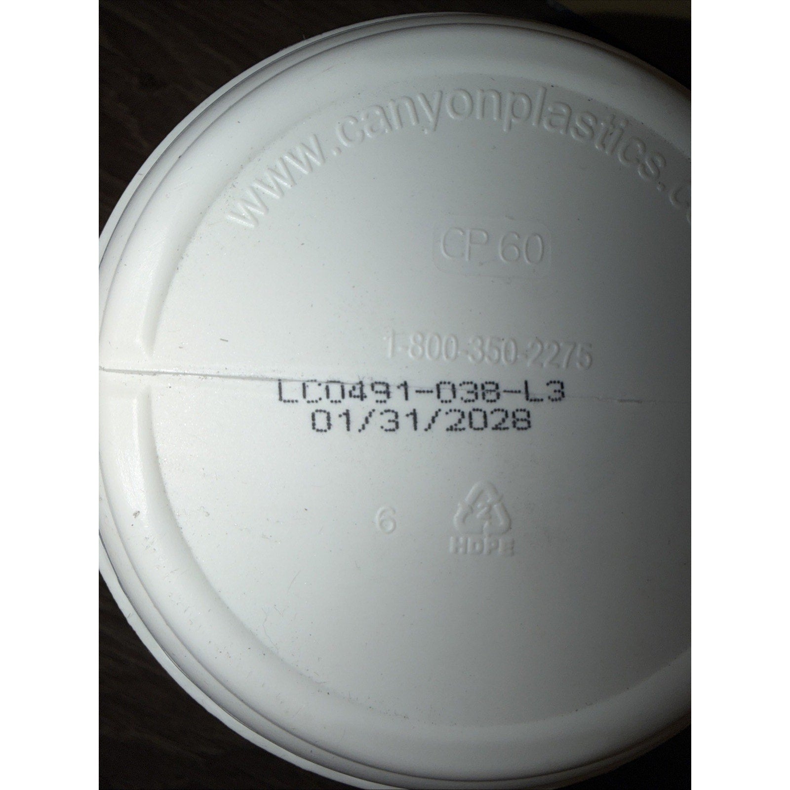 Close-up of a white plastic container lid showing embossed website, contact number, product code, expiration date, and recycling symbol for HDPE material.