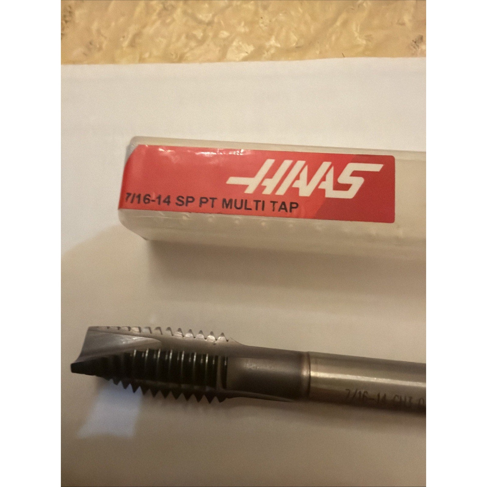 A single metal threading tap with sharp, multi-fluted cutting edges, displayed alongside a transparent plastic case with a red label marked "7/16-14 SP PT MULTI TAP.