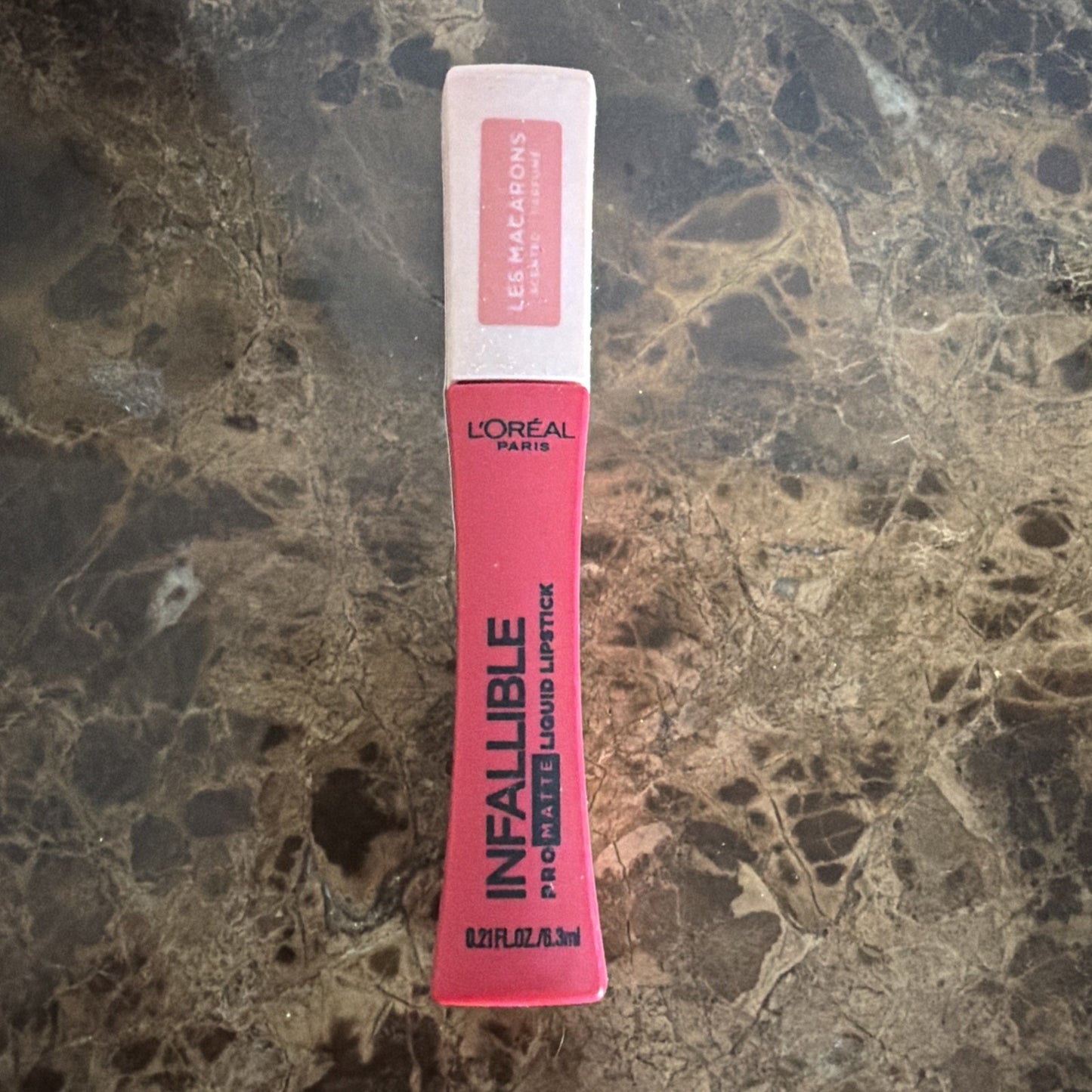 L'Oréal Paris Infallible Pro-Matte liquid lipstick in a bright pink shade with a white cap featuring the Les Macarons collection label, placed on a dark marble surface.
