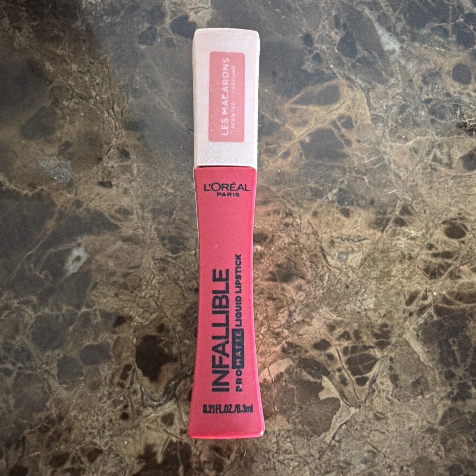 L'Oréal Paris Infallible Pro-Matte liquid lipstick in a bright pink shade with a white cap featuring the Les Macarons collection label, placed on a dark marble surface.