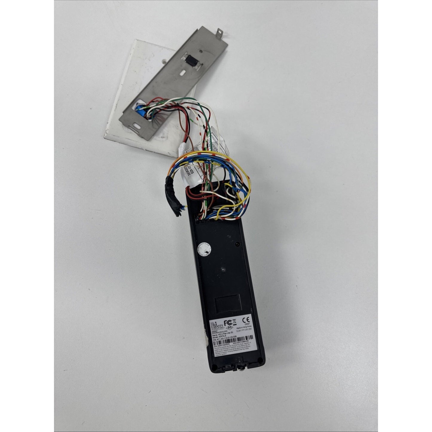 Black electronic device with multiple colored exposed wires connected to a rectangular metal plate, displayed on a plain white surface.