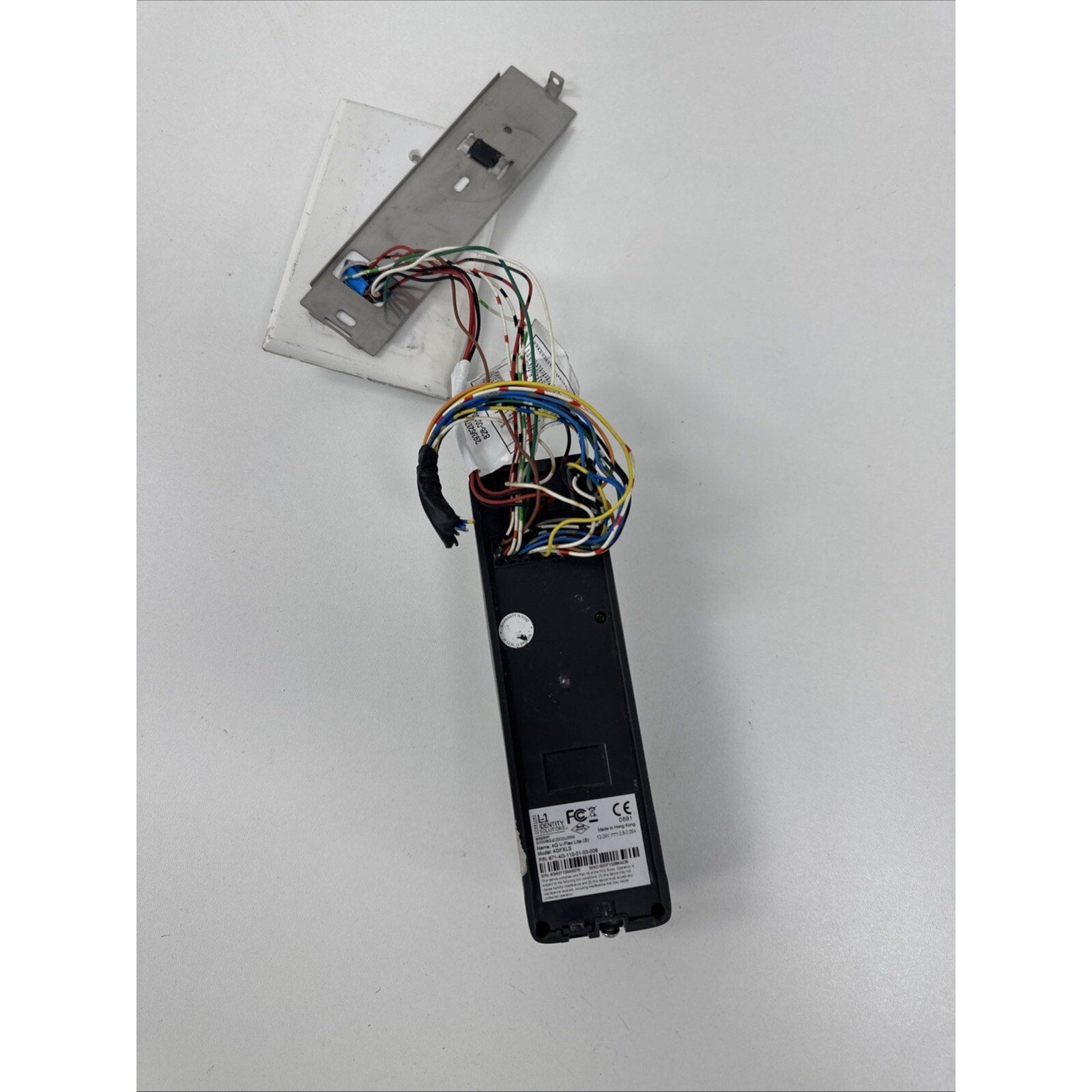 Black electronic device with multiple colored exposed wires connected to a rectangular metal plate, displayed on a plain white surface.