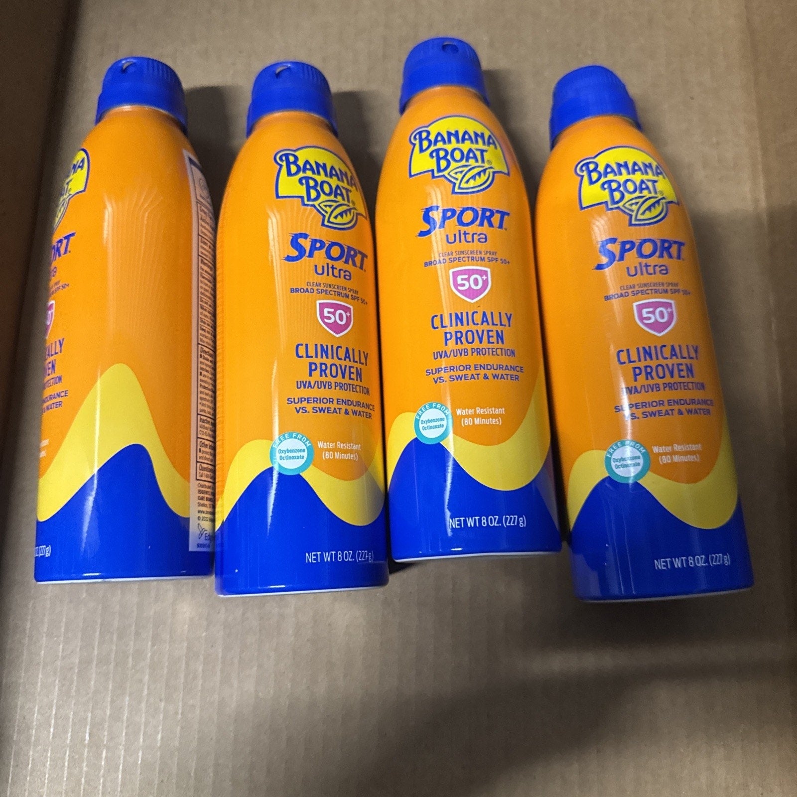 Four cans of Banana Boat Sport Ultra Sunscreen Broad Spectrum SPF 50 with blue caps in a cardboard box