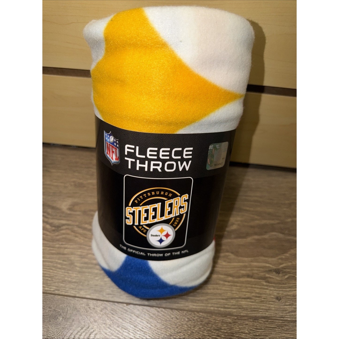 Rolled fleece throw blanket with a Pittsburgh Steelers logo on the black packaging label, featuring a white, yellow, and blue color pattern visible on the fabric.
