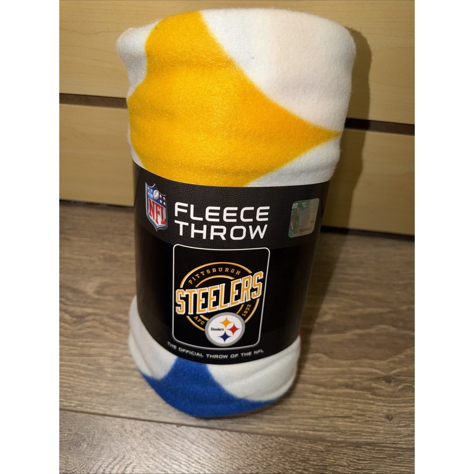 Rolled fleece throw blanket with a Pittsburgh Steelers logo on the black packaging label, featuring a white, yellow, and blue color pattern visible on the fabric.