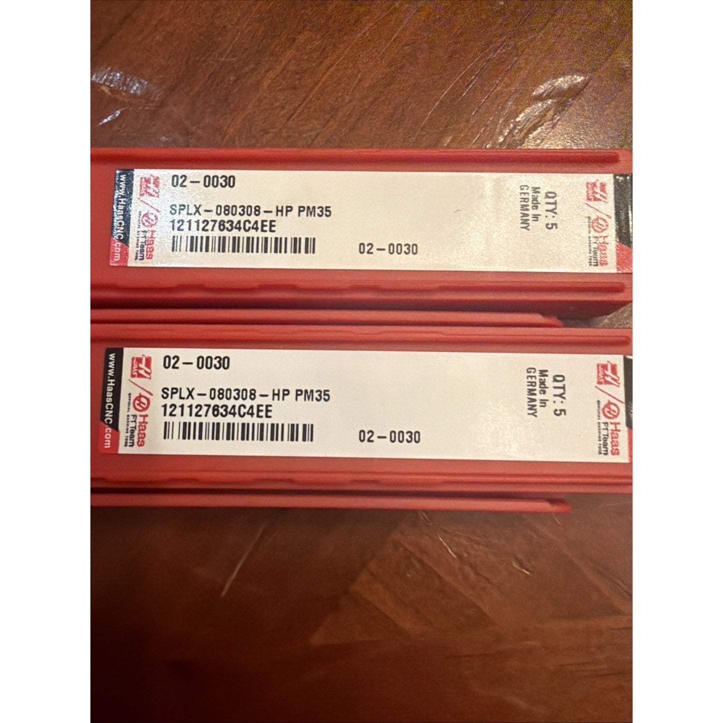 Two red rectangular packaging boxes with white labels displaying barcode, product code "SPLX-080308-HP PM35," quantity of 5, and "Made in Germany" printed, resting on a wooden surface.